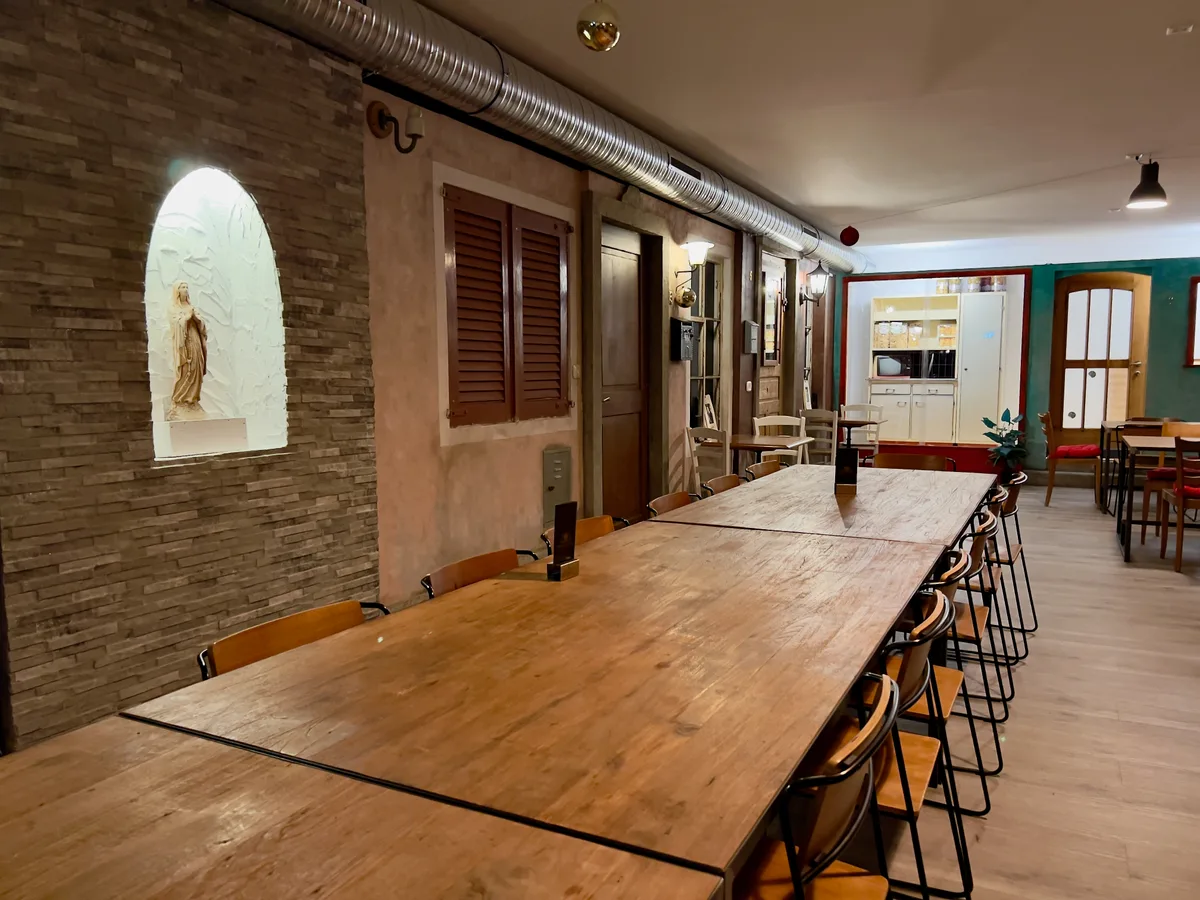 Man sieht mehrere bestuhlte Restauranttische aneinandergereiht in einem Raum. 